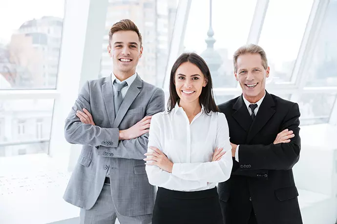 Ein Beraterteam lächelt die Kamera. Das Team besteht aus einer Frau, einem jungen Mann und einem älteren Mann.